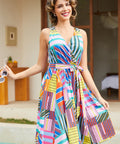 A woman wearing a sleeveless wrap-style midi dress with a colorful geometric patchwork print and v-neckline.