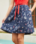 Woman wearing a navy skirt with mermaid pattern and a red top, standing by a pool.