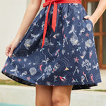 Woman wearing a navy skirt with mermaid pattern and a red top, standing by a pool.