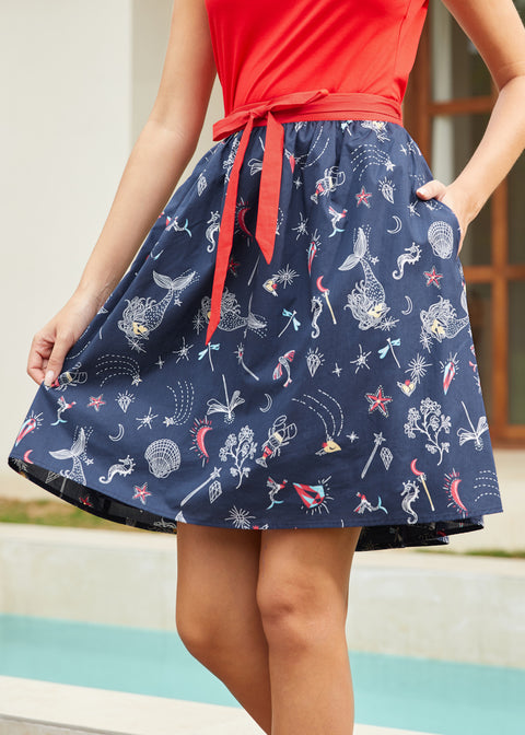 Woman wearing a navy skirt with mermaid pattern and a red top, standing by a pool.