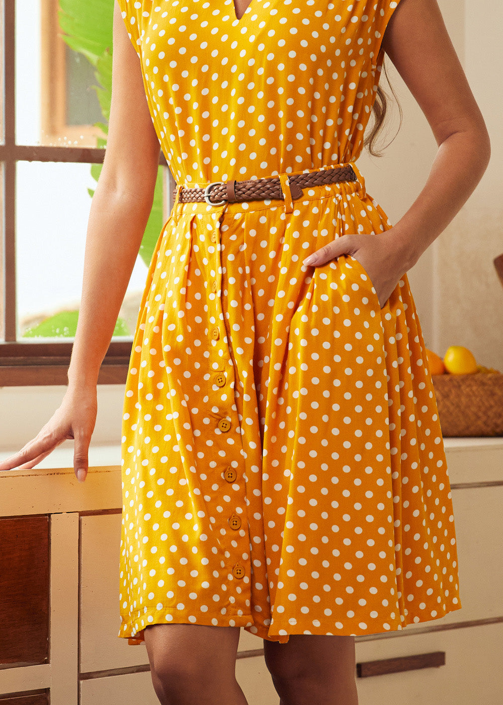 Woman wearing a yellow polka dot skirt with a belt in a kitchen setting
