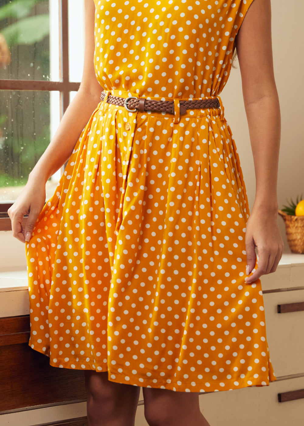 Woman wearing mustard yellow polka dot skirt with pockets and braided belt