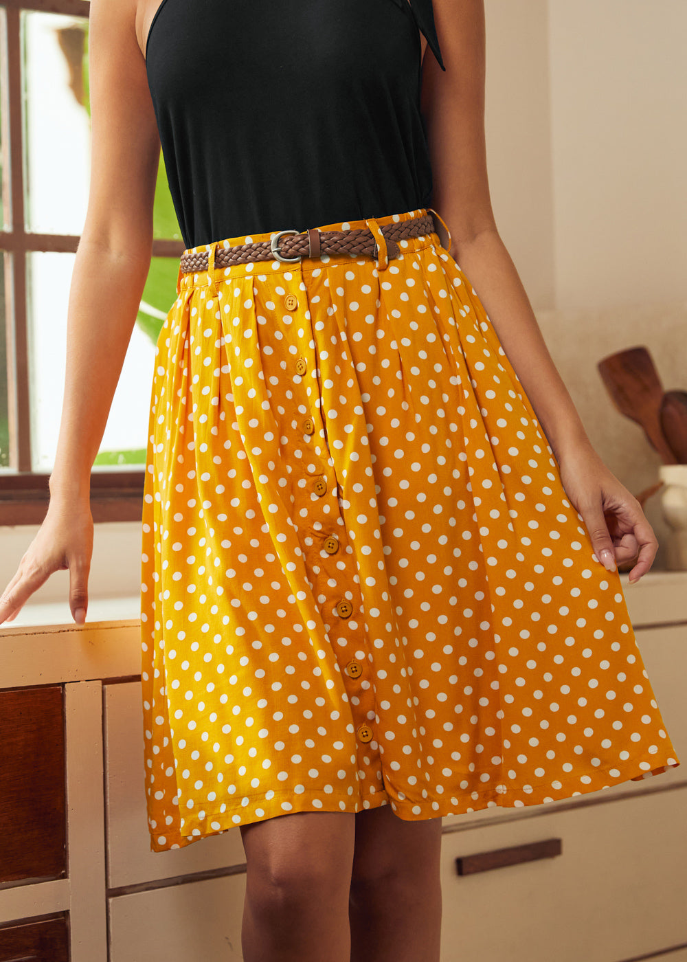 Woman wearing yellow polka dot knee-length skirt with braided belt and black sleeveless top