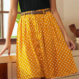 Woman wearing yellow polka dot knee-length skirt with braided belt and black sleeveless top