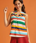Woman wearing a sleeveless rainbow striped cotton blouse with a camp collar and chest pocket.