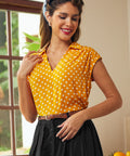 Woman wearing yellow polka dot blouse tucked into button-front skirt