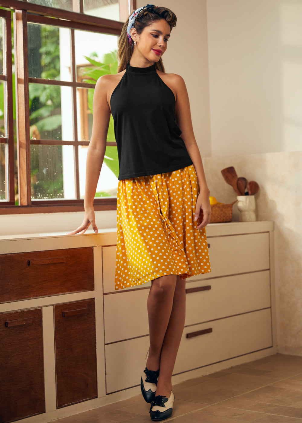 Full-length view of black sleeveless tie-neck top styled with yellow polka dot midi skirt