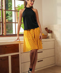 Full-length view of black sleeveless tie-neck top styled with yellow polka dot midi skirt