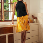 Full-length view of black sleeveless tie-neck top styled with yellow polka dot midi skirt