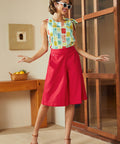 Model wearing red knee-length skort with high waist and button details styled with printed sleeveless top