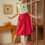 Model wearing red knee-length skort with high waist and button details styled with printed sleeveless top