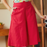 Woman wearing a colorful top and red skirt indoors.