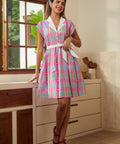 Woman wearing pink plaid fit and flare dress with white collar and waist tie, front view