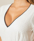 Close-up of white dress V-neckline with black ric rac trim detail