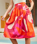 Person wearing a colorful skirt with abstract patterns by a poolside.