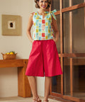 Woman wearing a colorful top and red shorts standing in a room with wooden furniture.