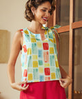 Woman wearing a colorful sleeveless top with a pattern of squares in various colors, standing indoors.