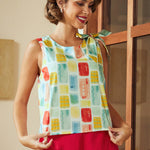 Woman wearing a colorful sleeveless top with a pattern of squares in various colors, standing indoors.