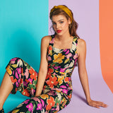 Woman sitting in colorful floral cropped jumpsuit with square neckline and wide-leg fit