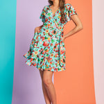 Woman wearing aqua fruit print wrap mini dress with flutter sleeves and tie waist