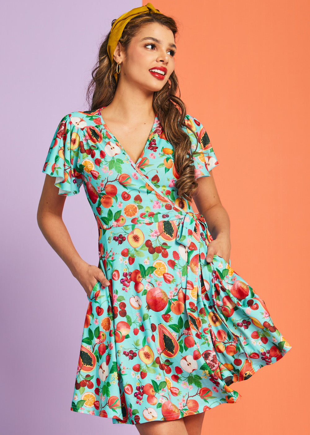 Woman wearing retro-inspired fruit print wrap dress with pockets and flutter sleeves