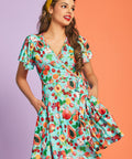 Woman wearing retro-inspired fruit print wrap dress with pockets and flutter sleeves