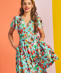 Front view of aqua wrap mini dress with fruit print and tie waist detail