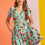 Front view of aqua wrap mini dress with fruit print and tie waist detail
