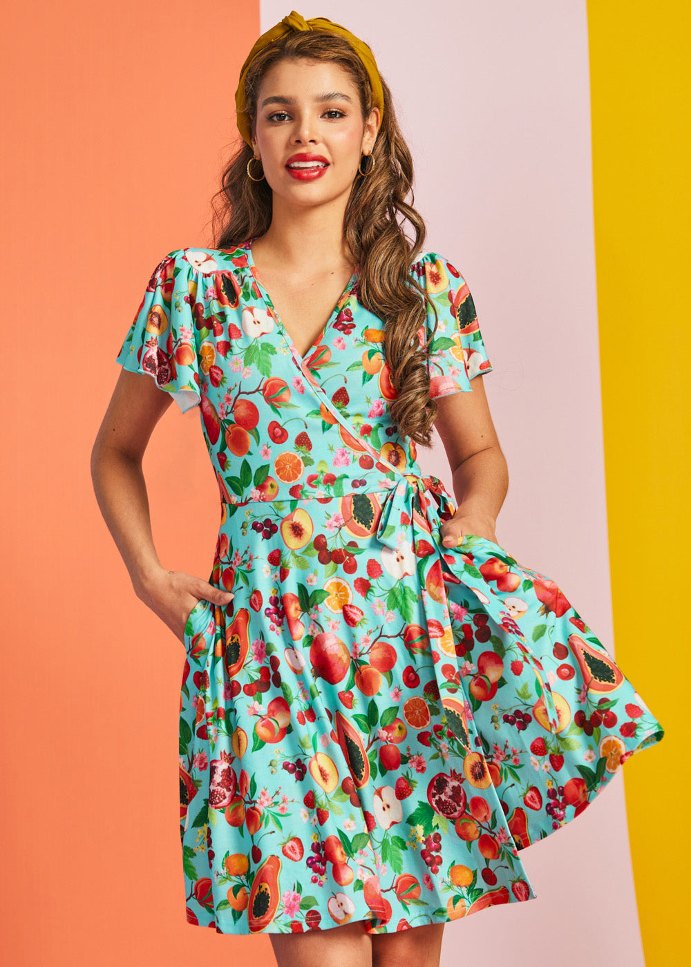 Front view of aqua wrap mini dress with fruit print and tie waist detail
