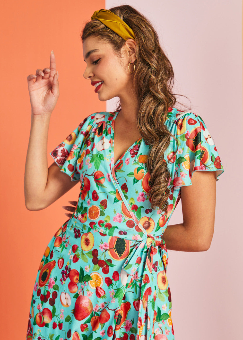 Woman wearing colorful fruit print wrap dress with flutter sleeves and vintage-inspired silhouette