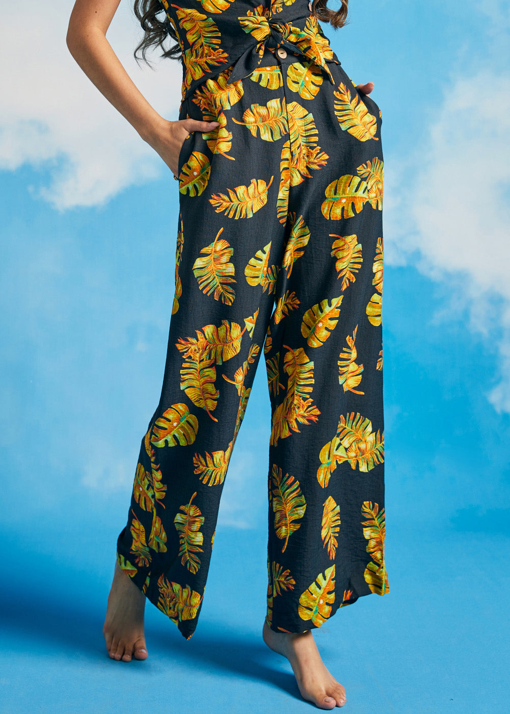 Woman wearing black pants with a yellow leaf pattern against a blue sky.