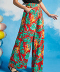 Woman wearing red tropical leaf pattern wide leg pants against a blue sky background