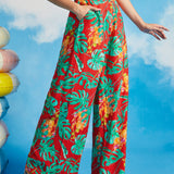 Woman wearing red tropical leaf pattern wide leg pants against a blue sky background