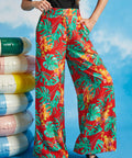 Woman wearing red tropical print pants with colorful flowers against a blue sky background.
