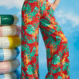 Woman wearing red tropical print pants with colorful flowers against a blue sky background.