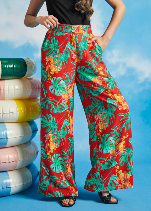 Woman wearing red tropical print pants with colorful flowers against a blue sky background.
