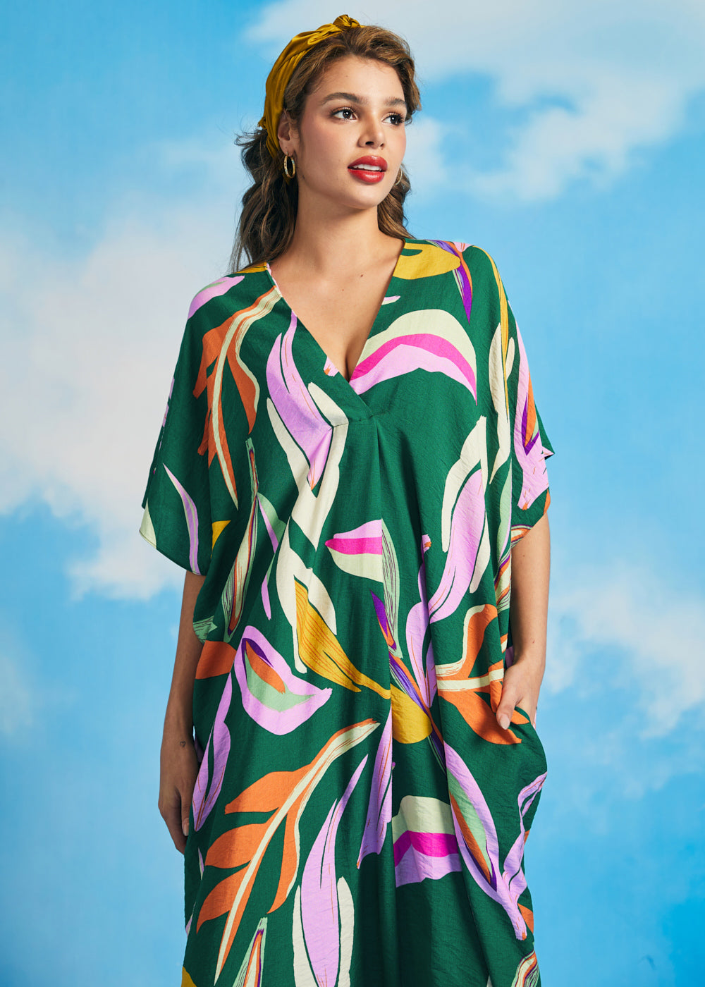 Woman posing in retro tropical maxi caftan dress with high-low hem and bold botanical print