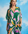 Woman posing in retro tropical maxi caftan dress with high-low hem and bold botanical print