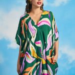 Woman posing in retro tropical maxi caftan dress with high-low hem and bold botanical print
