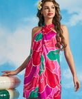 Woman in vibrant pink floral shift dress holding pastel pool float with retro resort styling