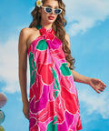Woman wearing pink tropical floral halter mini dress with twisted neckline and white cat-eye sunglasses