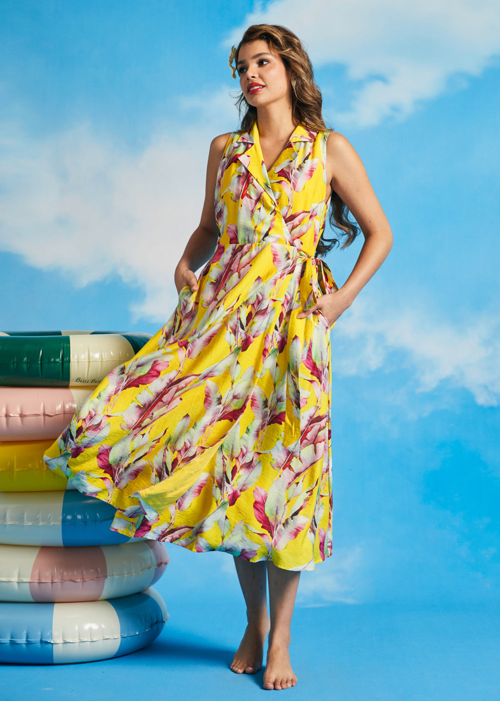 Woman wearing yellow tropical wrap midi dress with pockets and side tie detail