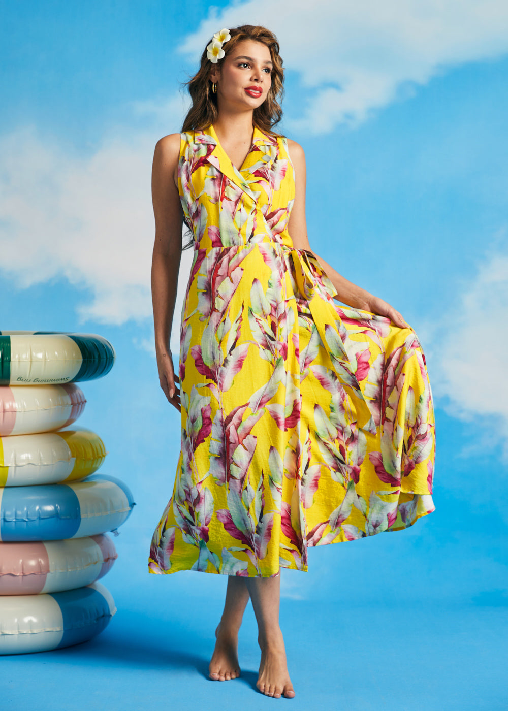 Woman holding skirt of yellow tropical leaf print wrap midi dress with pockets