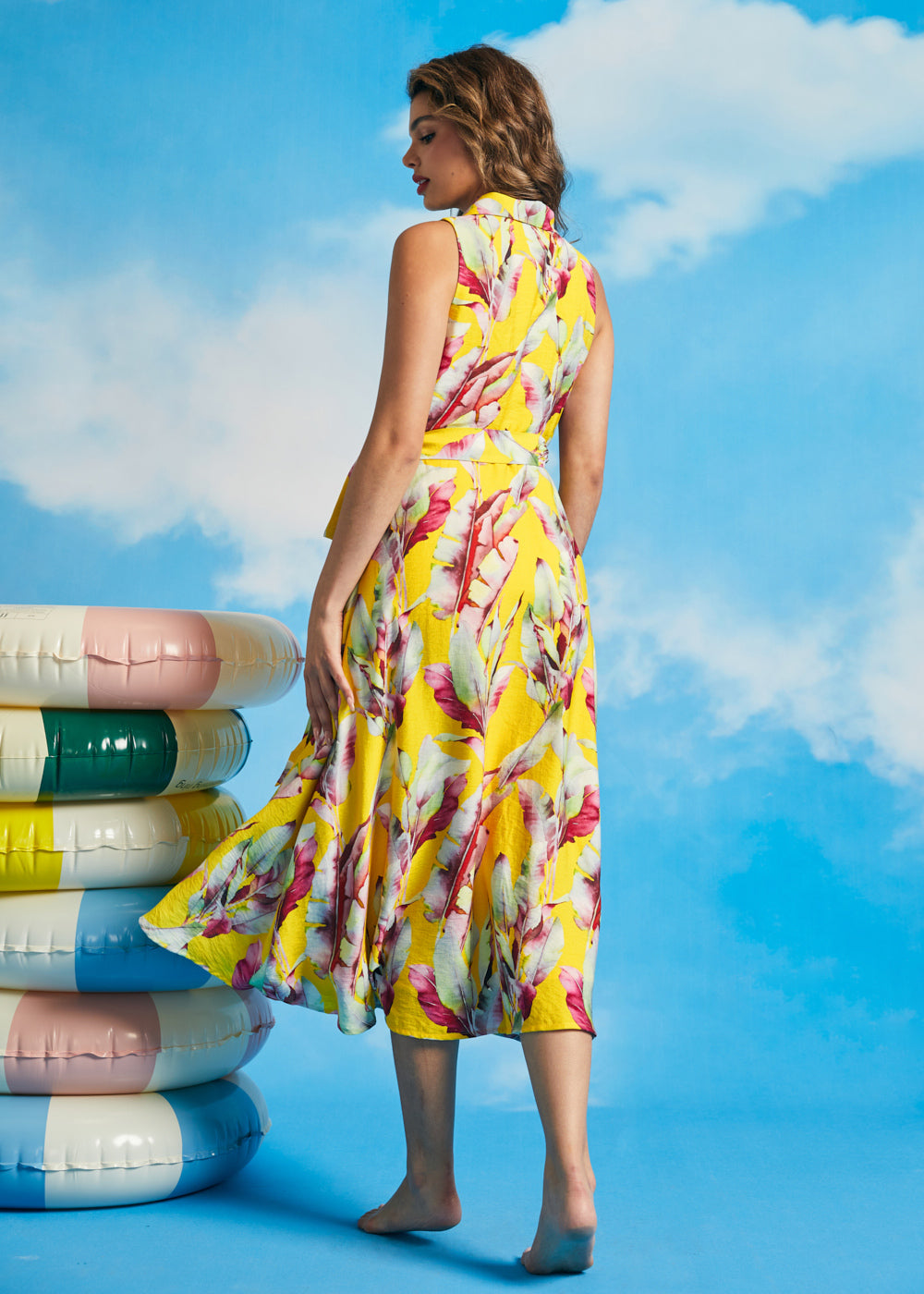 Back view of tropical yellow midi dress with sleeveless silhouette and flowing hem
