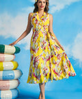 Woman wearing yellow tropical leaf print sleeveless wrap midi dress with tie waist and flowing skirt