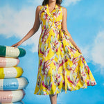 Woman wearing yellow tropical leaf print sleeveless wrap midi dress with tie waist and flowing skirt