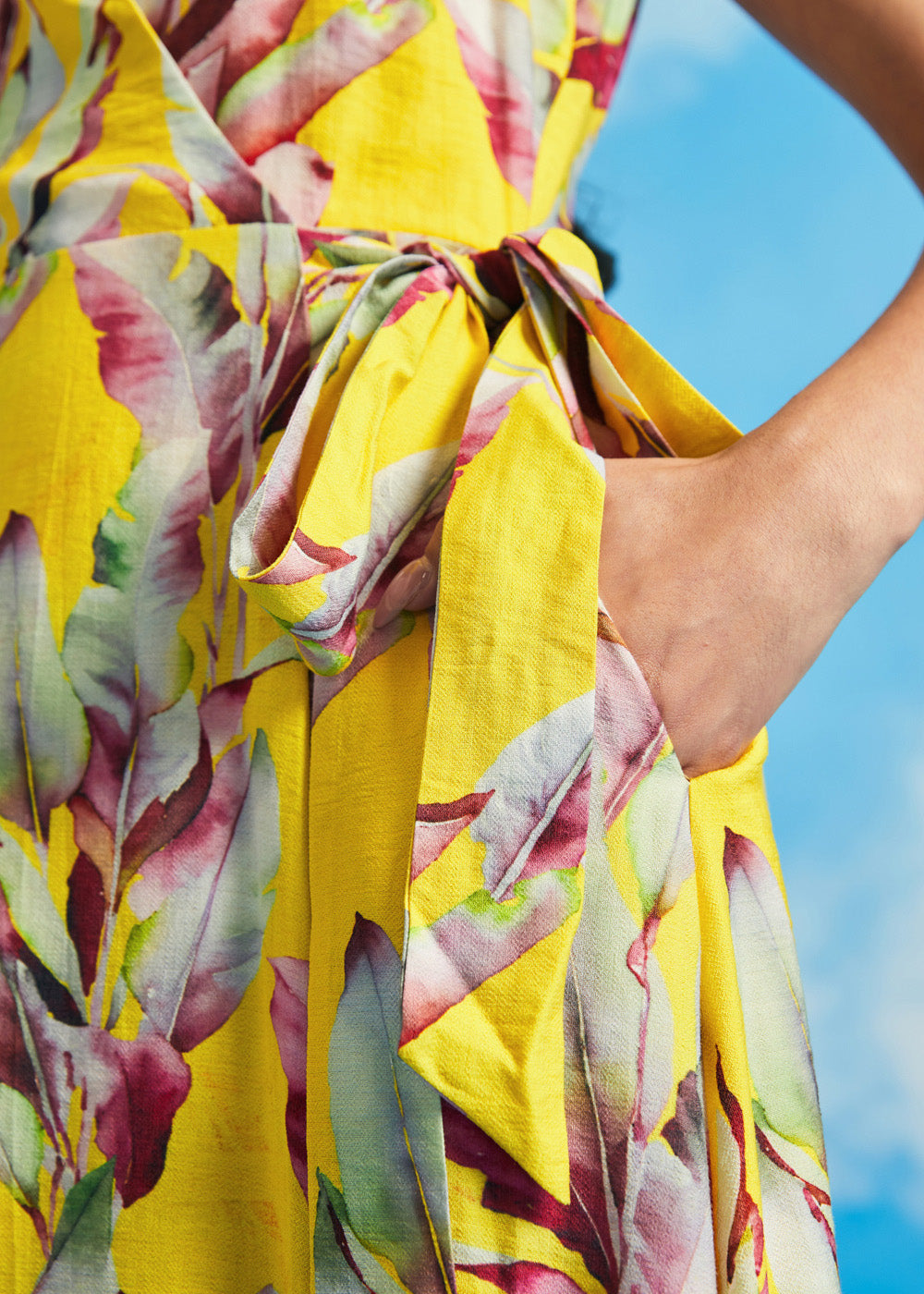 Close-up of tie waist detail on yellow tropical leaf print wrap midi dress