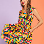 Woman twirling in colorful tropical leaf print sleeveless mini dress