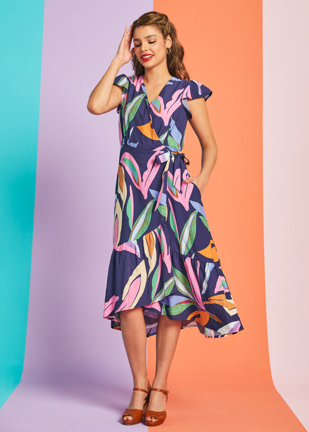 Woman wearing tropical abstract print midi wrap dress with flutter sleeves and asymmetrical hem