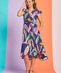 Woman wearing tropical abstract print midi wrap dress with flutter sleeves and asymmetrical hem